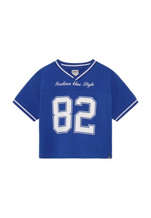 Blaues, kurz geschnittenes T-Shirt mit V-Ausschnitt, kurzen Ärmeln und der weißen Nummer „82“. Auf der Vorderseite steht in Weiß "Indian Blue Style".