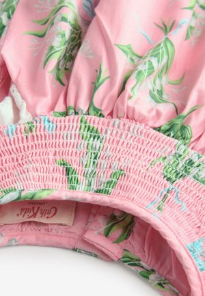 Tissu fleuri rose avec des feuilles vertes, présentant un smock élastique et une doublure blanche. Étiquette visible avec l'inscription "Cali Kids London." Texture douce en coton.