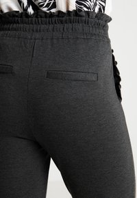 Grå midje-elastiska joggers med en slät yta, som har två bakfickor och en dekorativ volang längs sidorna.