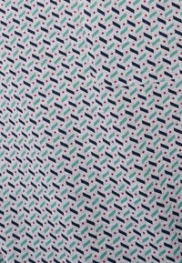 Tessuto decorato con un design geometrico che presenta accenti di blu scuro, verde e rosso su uno sfondo chiaro con forme e punti ripetuti.