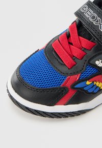 Dziecięcy tenisówka z niebieską siateczką, czarną i czerwoną skórą, czerwonymi sznurówkami, białą podeszwą i kolorowym logo z skrzydłami po boku.