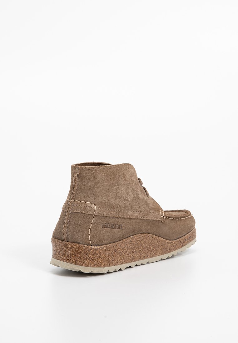 Bottine en daim marron avec un milieu de semelle en liège, des détails cousus et une semelle en caoutchouc. Présente un bout rond et une texture douce.