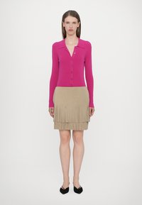 Top tricotat fucsia cu nasturi și guler, asociat cu o fustă bej cu franjuri. Prezintă mâneci lungi și un design de fustă în straturi. Se poartă cu balerini negri.