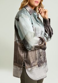 Lekka, wzorzysta bluzka w odcieniach aqua i szarości. Posiada zapinany na guziki przód, kołnierzyk oraz długie, marszczone rękawy z rozcięciem na dole.