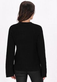 Pulover tricotat negru, cu mâneci lungi, guler rotund și slituri laterale la tiv. Materialul are un aspect texturat și voluminos.