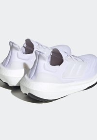 Paire de chaussures de course blanches avec semelles amortissantes et semelles extérieures noires, vues de dos et légèrement de dessus sur un fond uni.