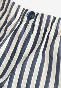 Shorts od prugaste tkanine s mornarsko plavim i kremastim vertikalnim prugama, elastičnim pojasom i tamnim izvezenim logotipom na pojasu.