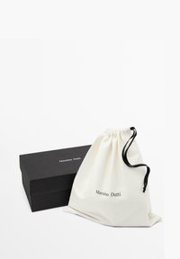 Baumwoll-Zugbeutel in Off-White mit schwarzen Akzenten neben einer schwarzen rechteckigen Box, beide mit dem "Massimo Dutti"-Logo.