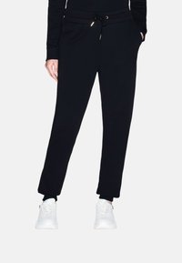 Pantaloni tuta neri con una vita regolabile con cordino, tasche laterali e polsini aderenti. Realizzati in un tessuto morbido con dettagli minimi.