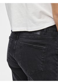 Svarte denimjeans med en tett design, med en baklomme og en merkevarelapp. Materialet har en lett tekstur og et falmet utseende.