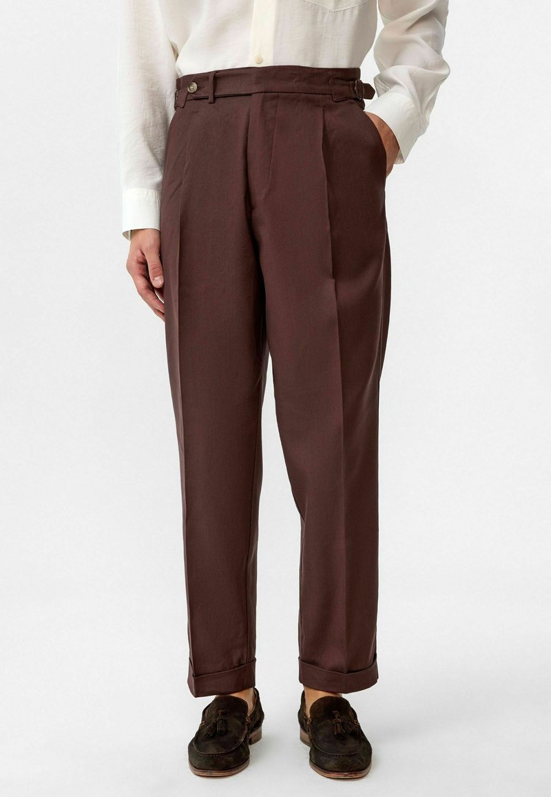 Bruine geplooide broek met een hoge taille, zijzakken en een wijd pijpdesign. Afgewerkt met een omgeslagen zoom en subtiele knoopdetails.