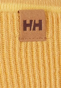 Tejido de punto amarillo con una textura acanalada, que presenta una etiqueta de cuero marrón con el logo "HH" en una fuente sencilla.