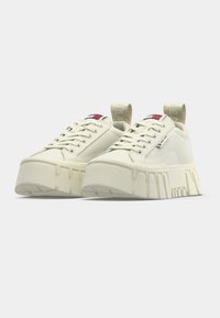 Αθλητικά παπούτσια σε κρεμ απόχρωση με χοντρή σόλα πλατφόρμας, διαθέτο υν σχέδιο με κορδόνια, διακριτικό λογότυπο και υφασμάτινη θηλιά στο τακούνι.