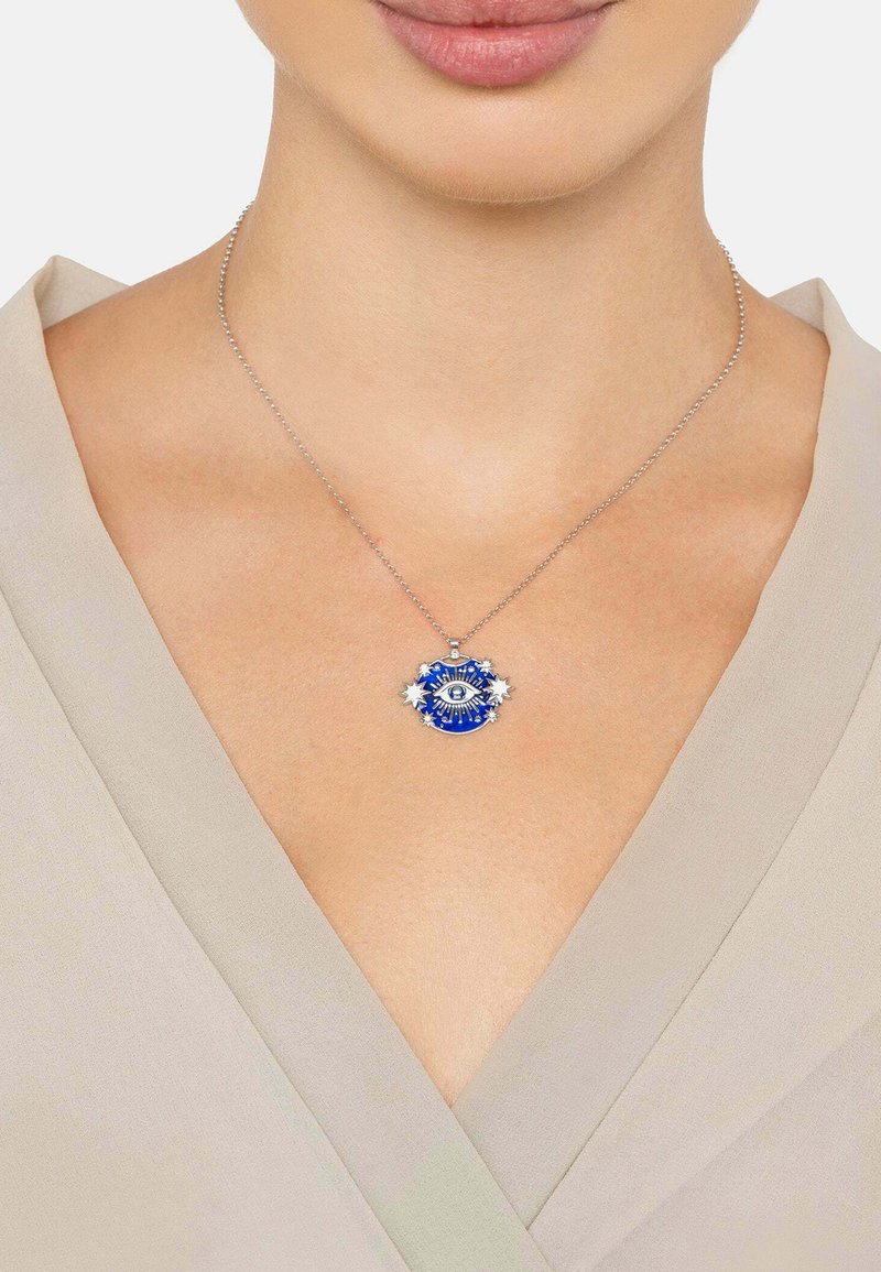 Hopeaketju kaulakoru, jossa on sininen riipus silmäsuunnittelulla, jota korostavat pienet tähdet, vaaleanharmaalla paidalla.