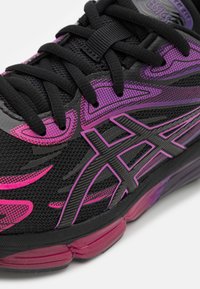 Black athletic shoe with pink and purple accents, featuring mesh upper, laces, and a durable rubber sole. Notable design elements include a streamlined shape.