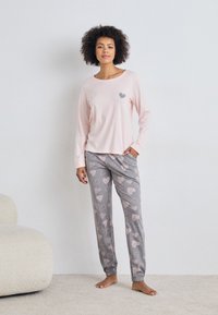 Ljusrosa långärmad topp med ett hjärtformad motiv över grå pyjamasbyxor med hjärtmönster. Mjuk tyg, lös passform, elastiska ärmmuddar.