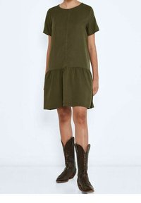 Vestido verde oliva de manga corta con dobladillo en capas, hecho de una tela suave. Combinado con botas vaqueras marrones con costuras decorativas.