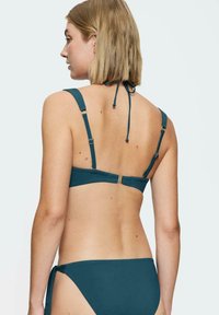 Turbia bikini w zestawie z regulowanymi ramiączkami, zapięciem na zamek i sznurkiem po bokach. Gładka tekstura i minimalistyczny design.