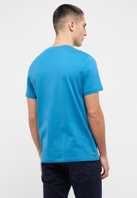 Short-sleeve crewneck t-shirt in vibrant blue cotton fabric, with a smooth texture and a relaxed fit, shown from the back.