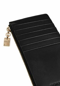 Schwarze Lederbrieftasche mit Reißverschluss, ausgestattet mit mehreren Kartenfächern, goldenen Reißverschlussbeschlägen und einem kleinen dekorativen Charm.
