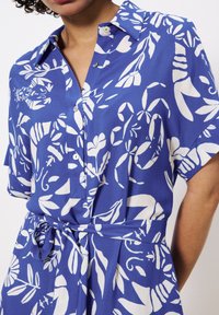 Blaues Hemdblusenkleid mit weißen Blumenmustern, kurzen Ärmeln und tailliertem Bund. Verfügt über einen klassischen Kragen und eine glatte Stofftextur.