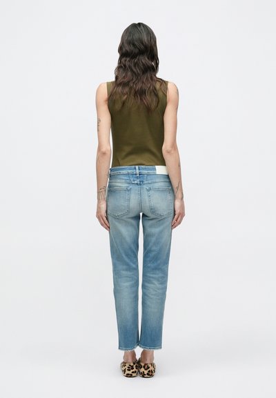 Haut vert sans manches, jean bleu clair et chaussures à motif animalier. Le jean présente une coupe décontractée et est légèrement usé au niveau de l'ourlet.