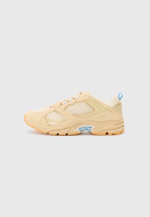 Beige athletic shoe featuring mesh and suede materials, prominent blue accents, textured rubber sole, and a rounded shape.