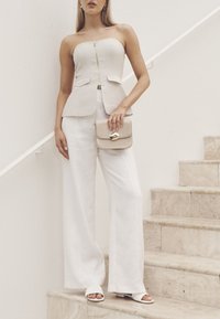 Beige strapless top with zip front, peplum detail; paired with wide-leg white pants. Holding a small beige bag with gold hardware.