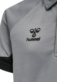 Grå polo med en texturerad yta, med en svart logotyp på bröstet. Detaljerna inkluderar en kontrasterande svart ärmtrim.