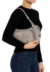 Borsa a spalla in suede grigio con dettagli in oro, dotata di una tasca frontale con zip e una forma arrotondata. La borsa viene indossata sotto il braccio.
