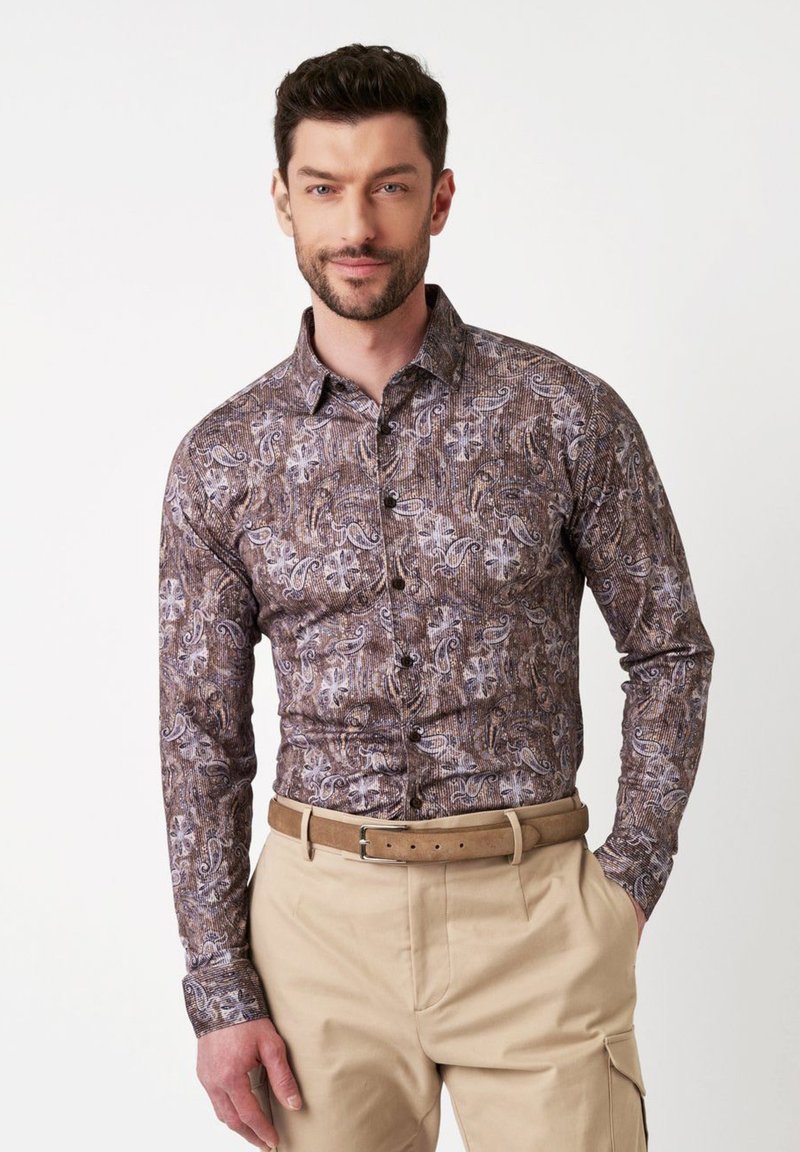 Bruine shirt met een paisley patroon, knoopsluiting aan de voorkant en lange mouwen. Gecombineerd met beige broek en een brede bruine riem.