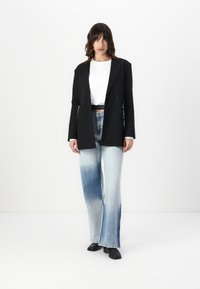 Črni krojen blazer čez belo majico, v kombinaciji z svetlo modrimi širokimi jeans hlačami z modrim gradientom. Črne čevlje dopolnjujejo outfit.