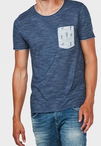 Marinblå t-shirt med kort ärm i en melerad textur, prydd med en ljusfärgad bröstficka med ett kaktusmönster.