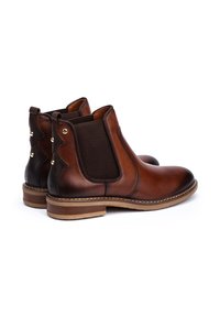 Paire de bottines Chelsea en cuir marron avec panneaux latéraux élastiques, talons en bois empilés et détails en clous métalliques à l'arrière.