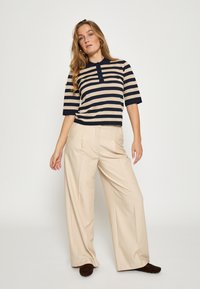 Beige og marineblå stribet kortærmet polo skjorte kombineret med beige bukser med vide ben. Outfittet har krave og knaplukning.