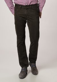 Donkergroene chino's met een gladde textuur, rechte snit en vijfzakkenontwerp, gecombineerd met grijze schoenen met blauwe accenten.