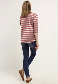 Rood-wit gestreepte 3/4 mouwen top van breigaren, gecombineerd met donkerblauwe strakke jeans en bruine gevlochten flats, gezien van achteren.