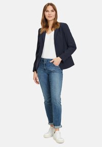 Námořnický blazer přes bílý tričko, spárovaný s světle modrými ohrnutými džíny a bílými teniskami. Hladká tkanina, dobře padnoucí střih a jednoduché knoflíky.