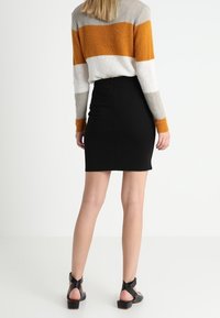 Schwarzer Bleistiftrock kombiniert mit einem gestreiften Pullover in Grau, Orange und Weiß. Hat lange Ärmel und ein körperbetontes Design. Pfennigabsatzsandalen.
