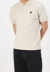 Polo shirt beige clair en coton avec un col classique et des manches courtes. Doté d'un petit patch logo sur la poitrine.
