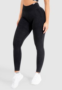 Leggings neri a vita alta realizzati in materiale testurizzato, con una cintura a coste e una silhouette liscia, abbinati a scarpe da ginnastica bianche.