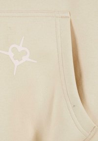 Sudadera de algodón beige con bolsillo frontal, decorada con un diseño en forma de corazón rosa claro y líneas radiales. Textura suave con costuras visibles.