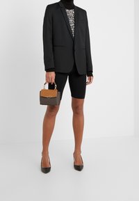 Czarna marynarka na topie w panterkę, zestawiona z czarnymi krótkimi spodenkami rowerowymi i czarnymi szpilkami. Trzyma małą brązową torebkę z wzorem.