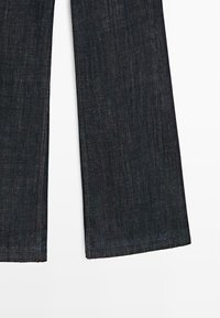 Jeans in denim scuro a gamba larga con orlo grezzo e texture sottile. Presentano cuciture a contrasto e nessuna ferramenta visibile.