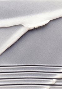Dikke witte crème, gelaagd op een gladde grijze ondergrond, met subtiele groeven en een golfachtige textuur, waardoor een visueel aantrekkelijk contrast ontstaat.