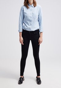 Ljusblå skjorta med knappar och långa ärmar, bröstficka, i kombination med svarta skinny jeans och svarta snörskor. Släta texturer, åtsittande design.