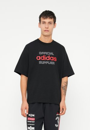 Črna bombažna majica s kratkimi rokavi, z napisom "URADNO" in "adidas DOBAVITELJ" natisnjenim v rdeči in beli barvi spredaj.