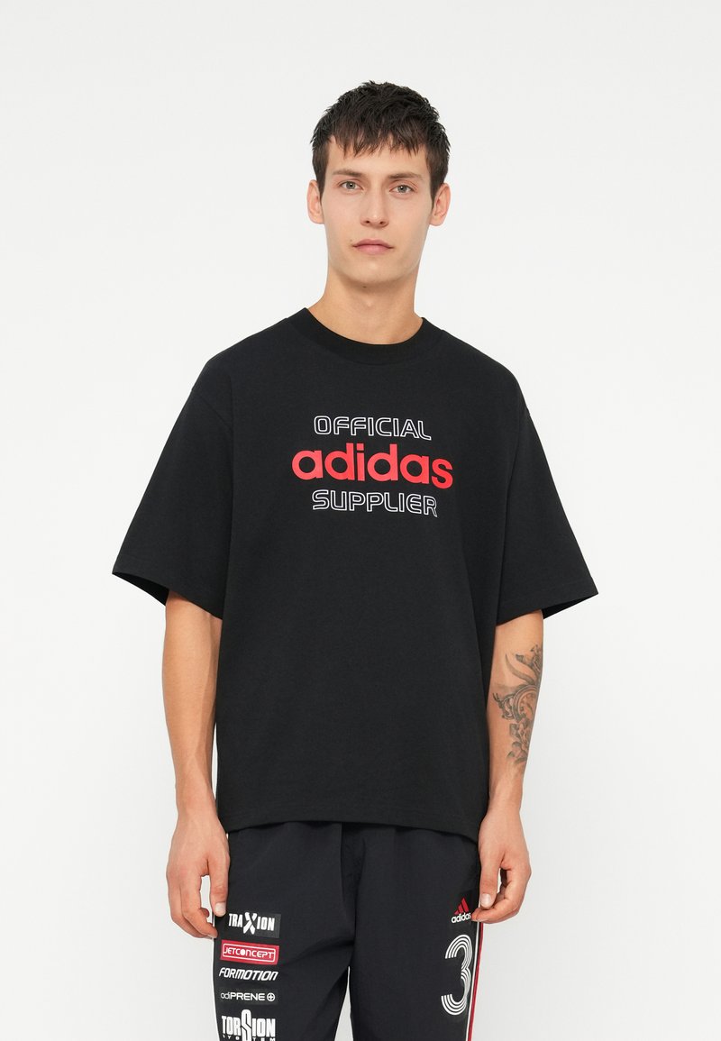 Melnas kokvilnas T-krekls ar īsām piedurknēm, uz kura priekšpuses sarkana un balta tekstā ir uzraksts "OFICIALS" un "adidas PIEGĀDĀTĀJS".
