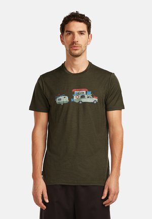 Mann trägt ein dunkelgrünes T-Shirt mit einer Grafik eines weißen Lastwagens, der einen Wohnwagen zieht, beide beladen mit Campingausrüstung, vor einem schlichten Hintergrund.
