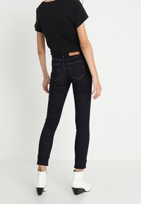 Smala mörka denimjeans med mid-rise passform, fem fickor och en brun läderetikett på baksidan, parat med vita ankelstövlar.